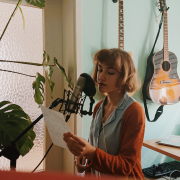 Anna Naumenko in the studio singing vocals into a microphone with guitars hanging on the wall