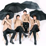 Rubber Soul Beatles tribute sitting down in their Shea Stadium jackets, holding black umbrellas