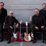 Tinos from Finland pose in black suits around a vox amp with their guitars